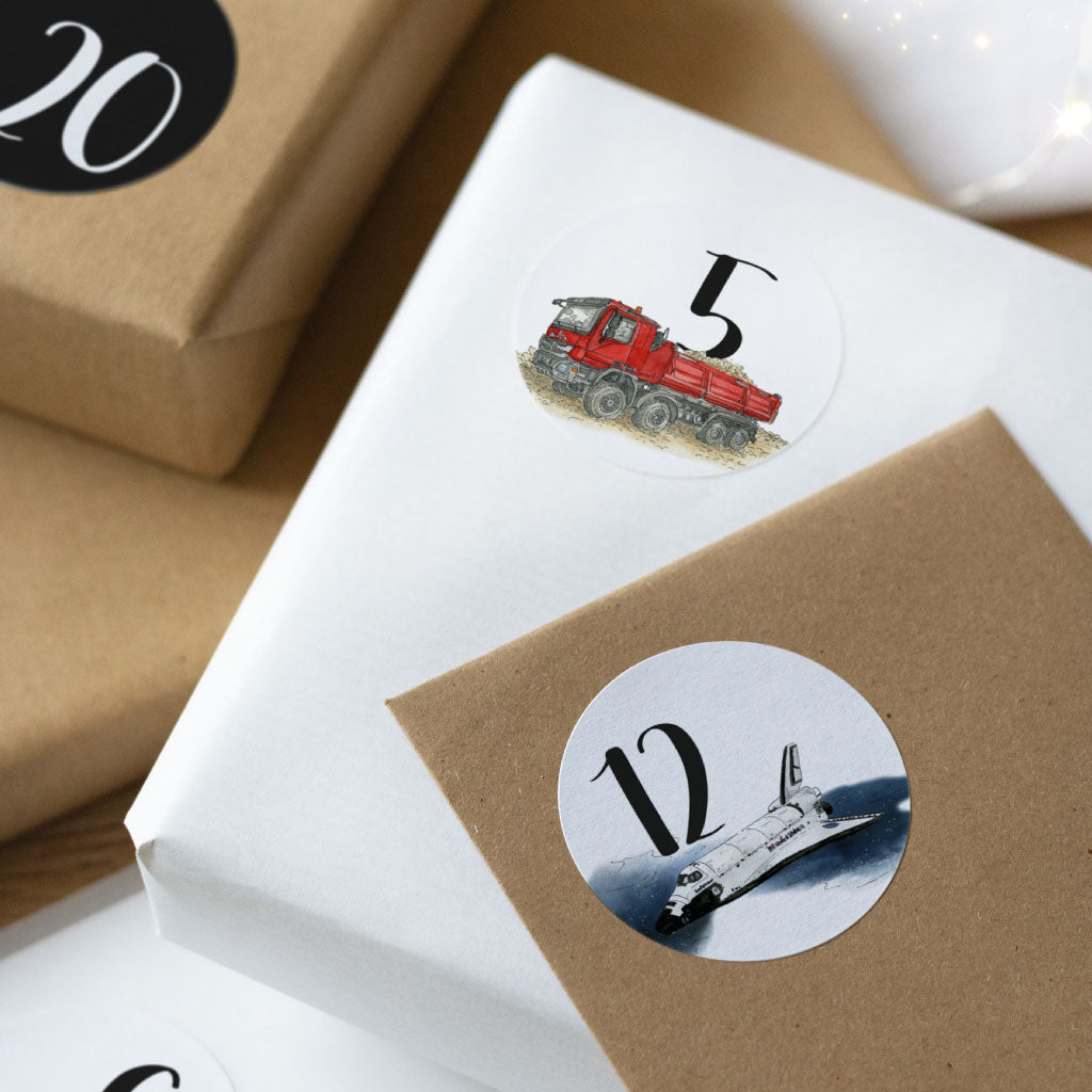 Detailfoto des runden Stickers 12 mit einem Space Shuttle und der Nummer 5 mit einem Kipper, aufgeklebt auf kleinen weißen und braunen Geschenken.