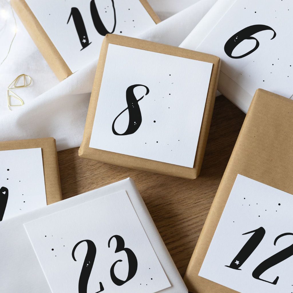 Adventskalender Kärtchen mit den Zahlen 8, 23, 12, 10 und 6 sind auf weißen und braunen kleinen Geschenken aufgeklebt