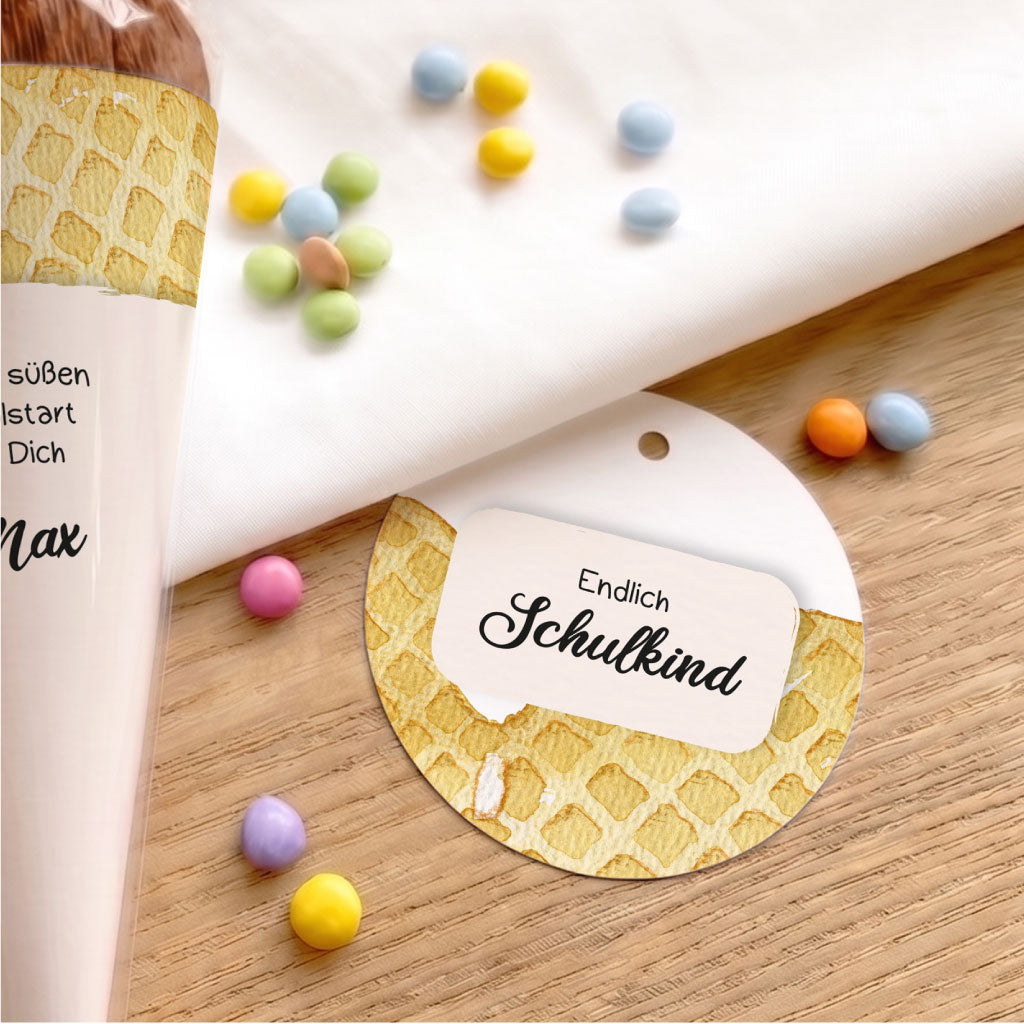 Runder Anhänger mit Waffel Aquarell Motiv neben kleiner Schultüte auf hellem Holzgrund.