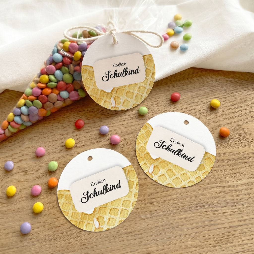 Drei runde Geschenkanhänger mit Waffel Aquarell Motiv und Text Endlich Schulkind auf Holzoberfläche.