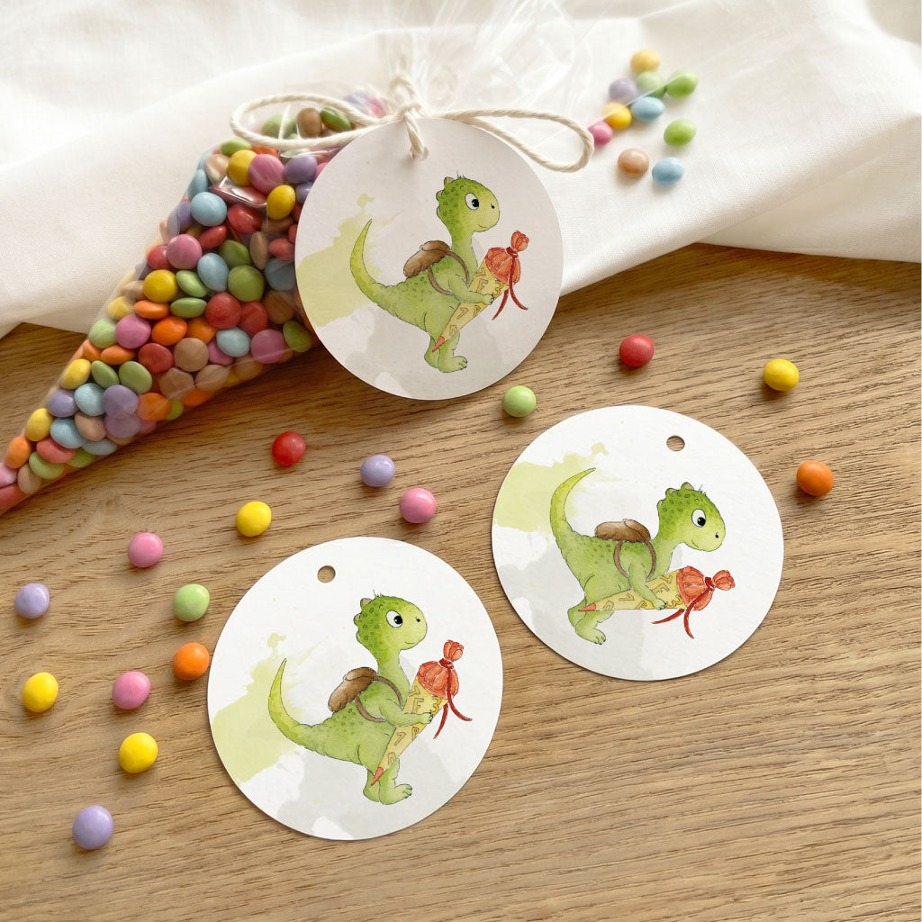 Drei runde Anhänger zur Einschulung mit Dino Aquarell Motiv und bunte Schokodrops auf hellem Hintergrund.