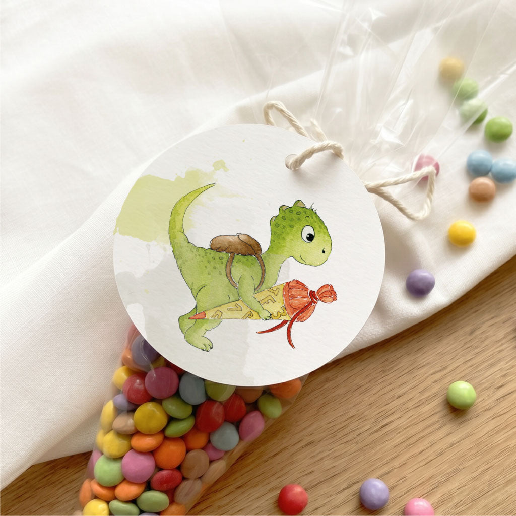 Nahaufnahme Anhänger zur Einschulung handgemaltes Dino Aquarell Motiv mit Schnur an Gastgeschenk befestigt.