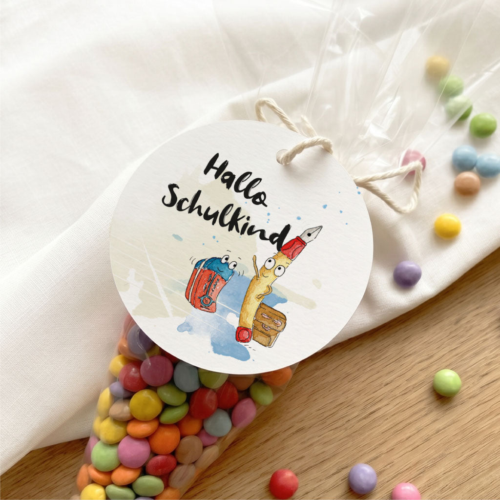 Nahaufnahme eines runden Geschenkanhängers für die Einschulung mit lustigem Füller und Ranzen Aquarell Motiv.