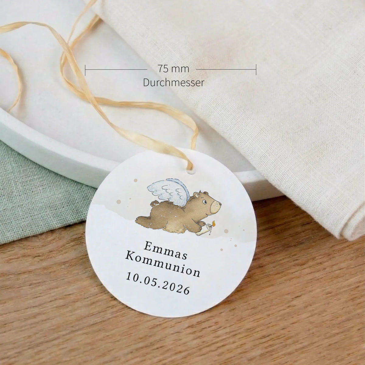Runder personalisierter Kommunion-Anhänger mit Aquarell Motiv Engelbär, 75 mm Durchmesser, mit Satinband auf Holzoberfläche.
