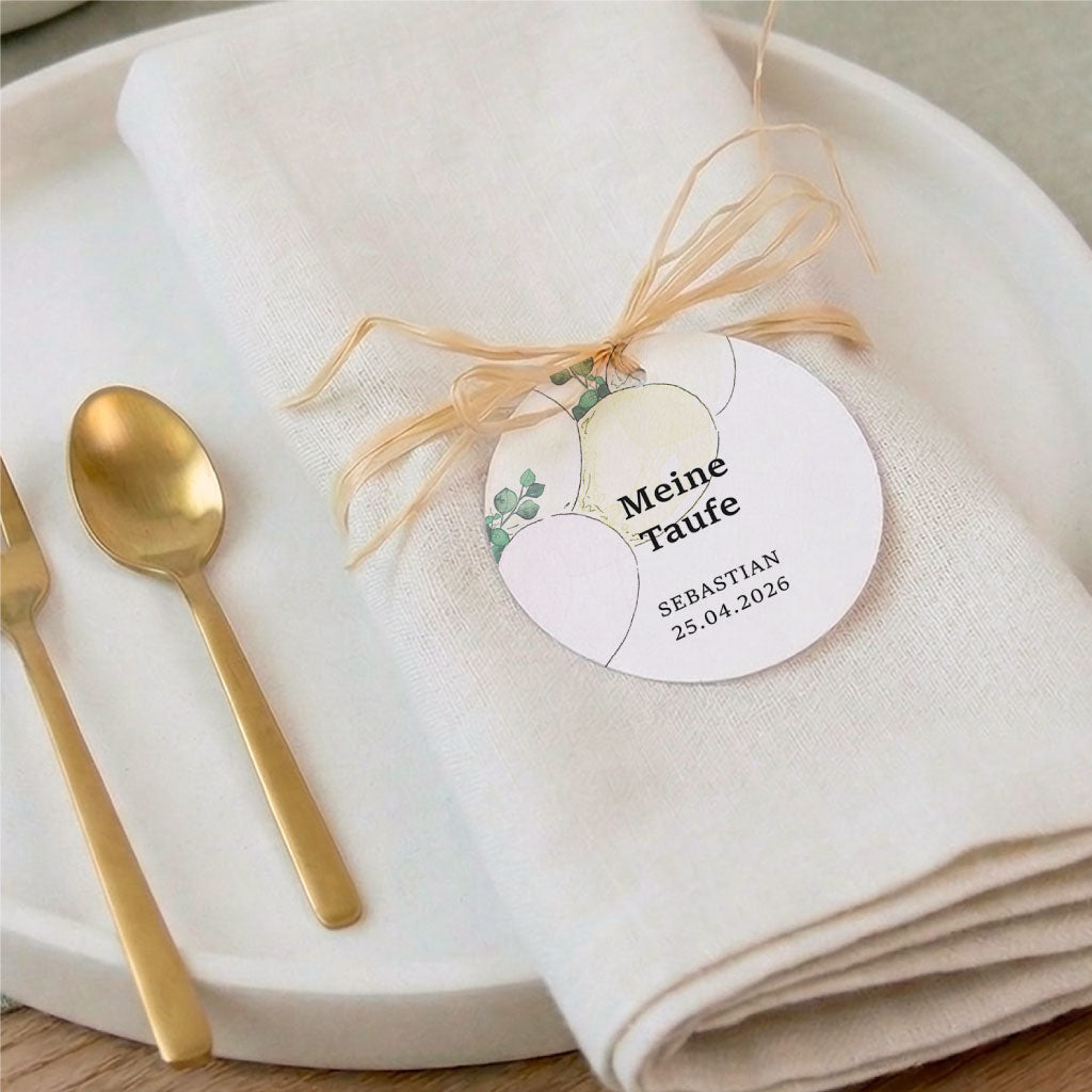 Elegante Tischdeko für die Tauffeier mit einem runden Anhänger an einer Stoffserviette und goldenen Elementen.