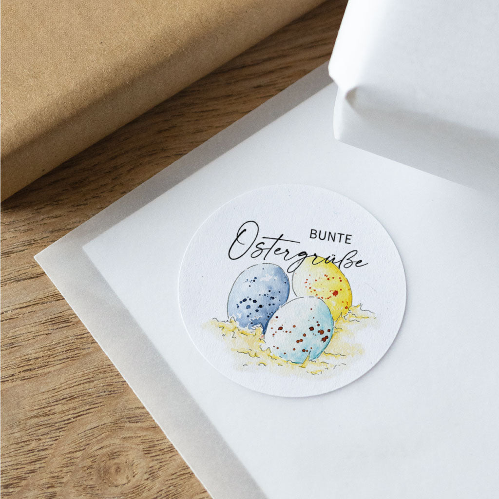 Runder Osteraufkleber mit Schriftzug „Bunte Ostergrüße“ und gemalten Ostereiern, Sticker für Ostern zum Verzieren von Geschenkverpackung und Deko.