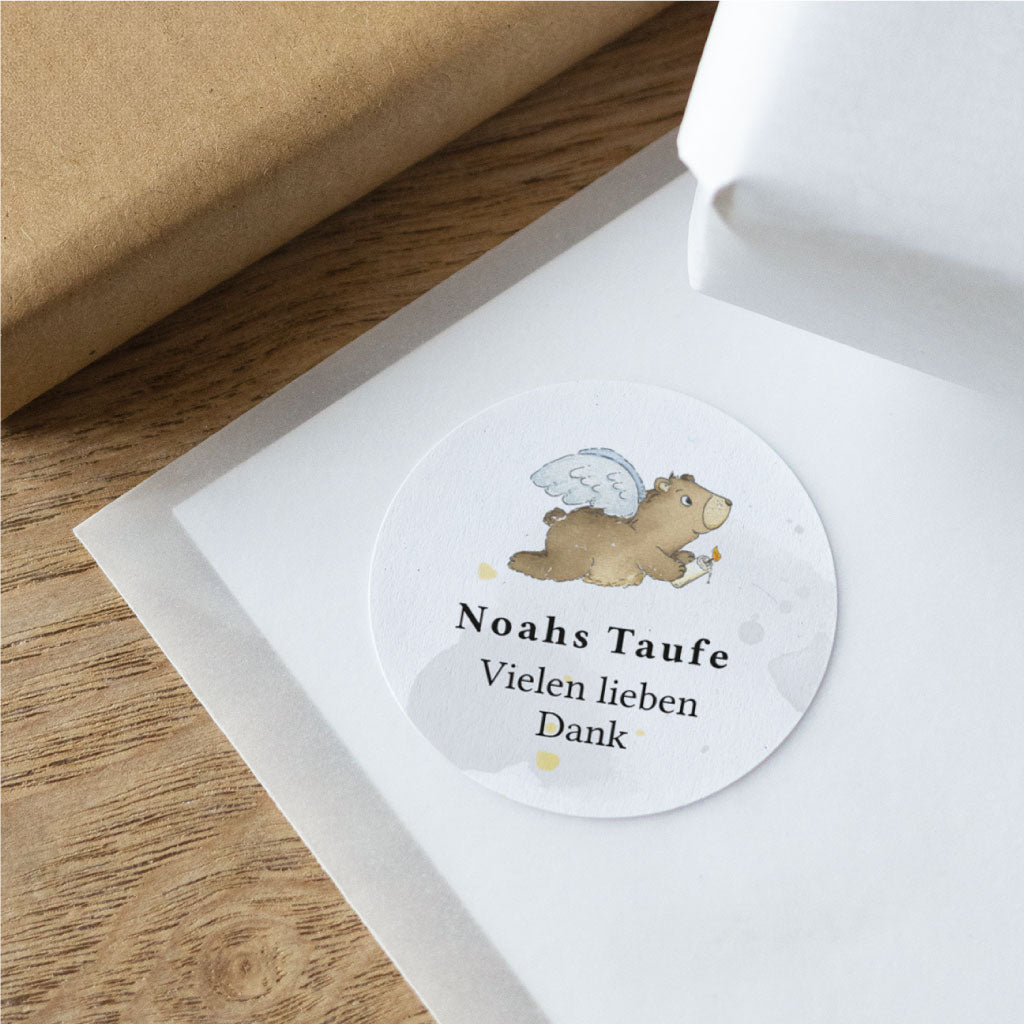Nahaufnahme eines personalisierten Stickers zur Taufe auf strukturiertem Papier mit handgemaltem Engelsbär Motiv