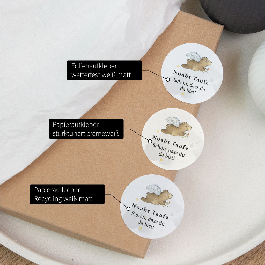 Vergleich von drei Materialien für personalisierte Taufe Aufkleber mit handgemaltem Motiv auf Folienaufkleber, Papieraufkleber und Recyclingpapier.