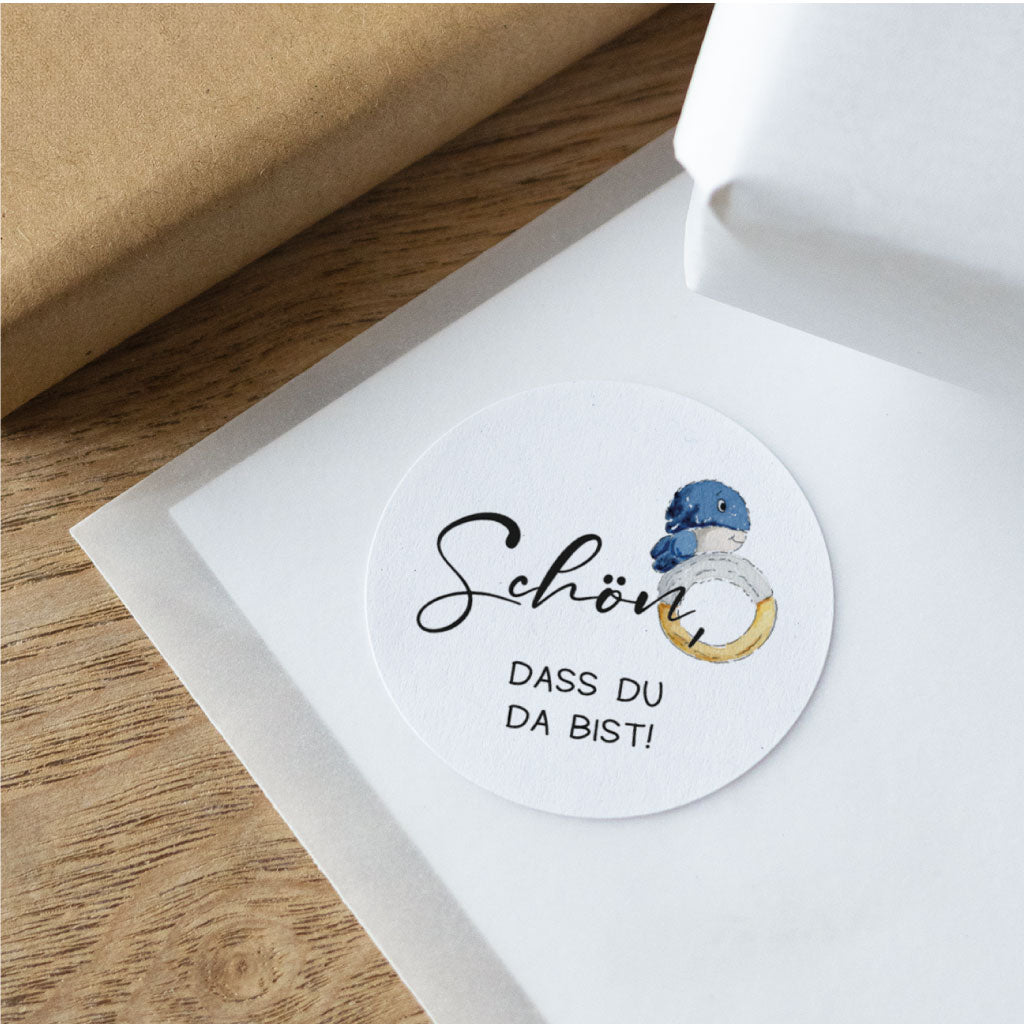 Detailansicht eines runden Stickers zur Taufe mit handgemaltem Wal und Schriftzug Schön, dass du da bist, auf hellem Untergrund