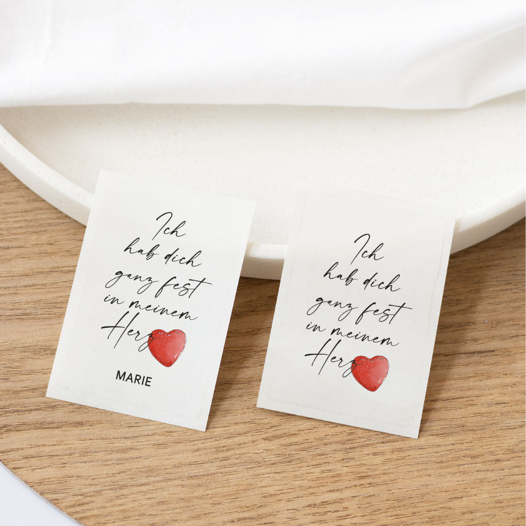 Zwei transparente Aufkleber mit dem Spruch „Ich hab dich ganz fest in meinem Herz“ und rotem Aquarell-Herz – einer davon mit Personalisierung – ideal für Grabkerzen und als liebevolles Andenken.