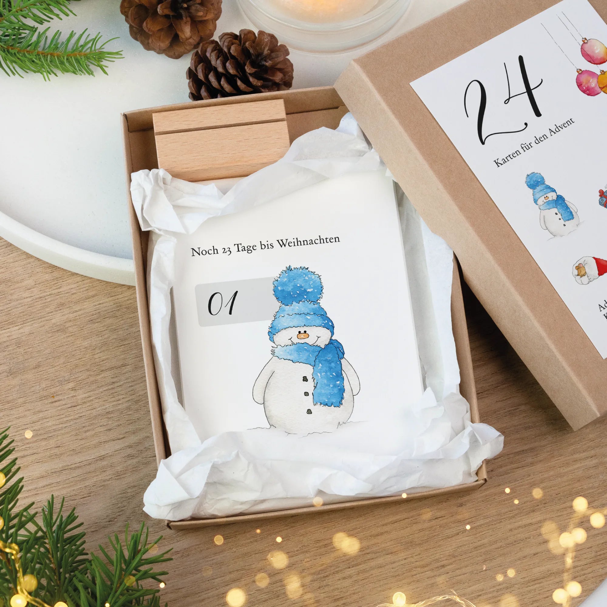 Offene Kraftkarton Schachtel mit Adventskalender Karten, Holz Kartenhalter und Schneemann Aquarell Motiv.