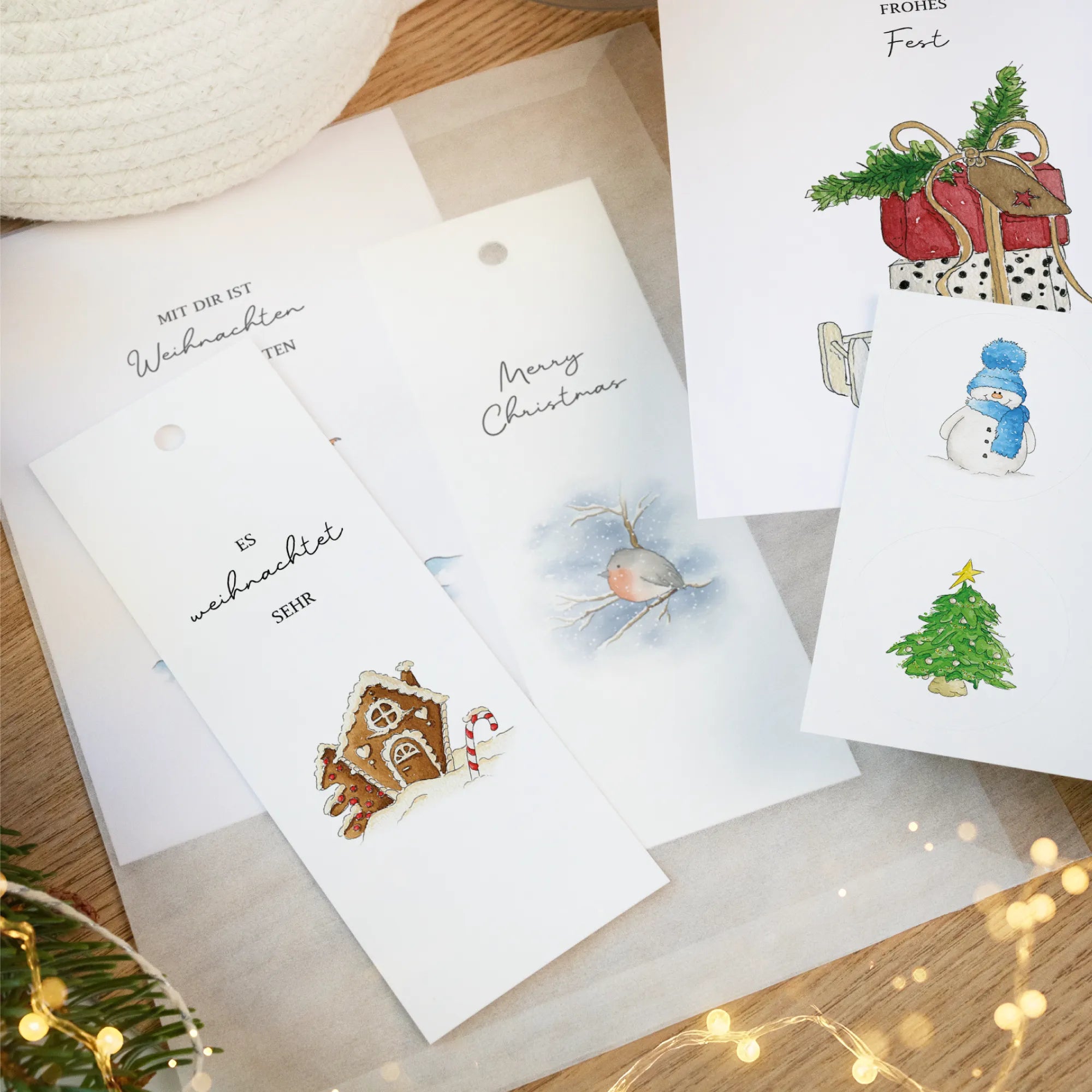Nahaufnahme von weihnachtlichen Anhängern und Aufklebern mit Aquarell Motiven wie Schneemann und Lebkuchenhaus auf einer Pergaminhülle.