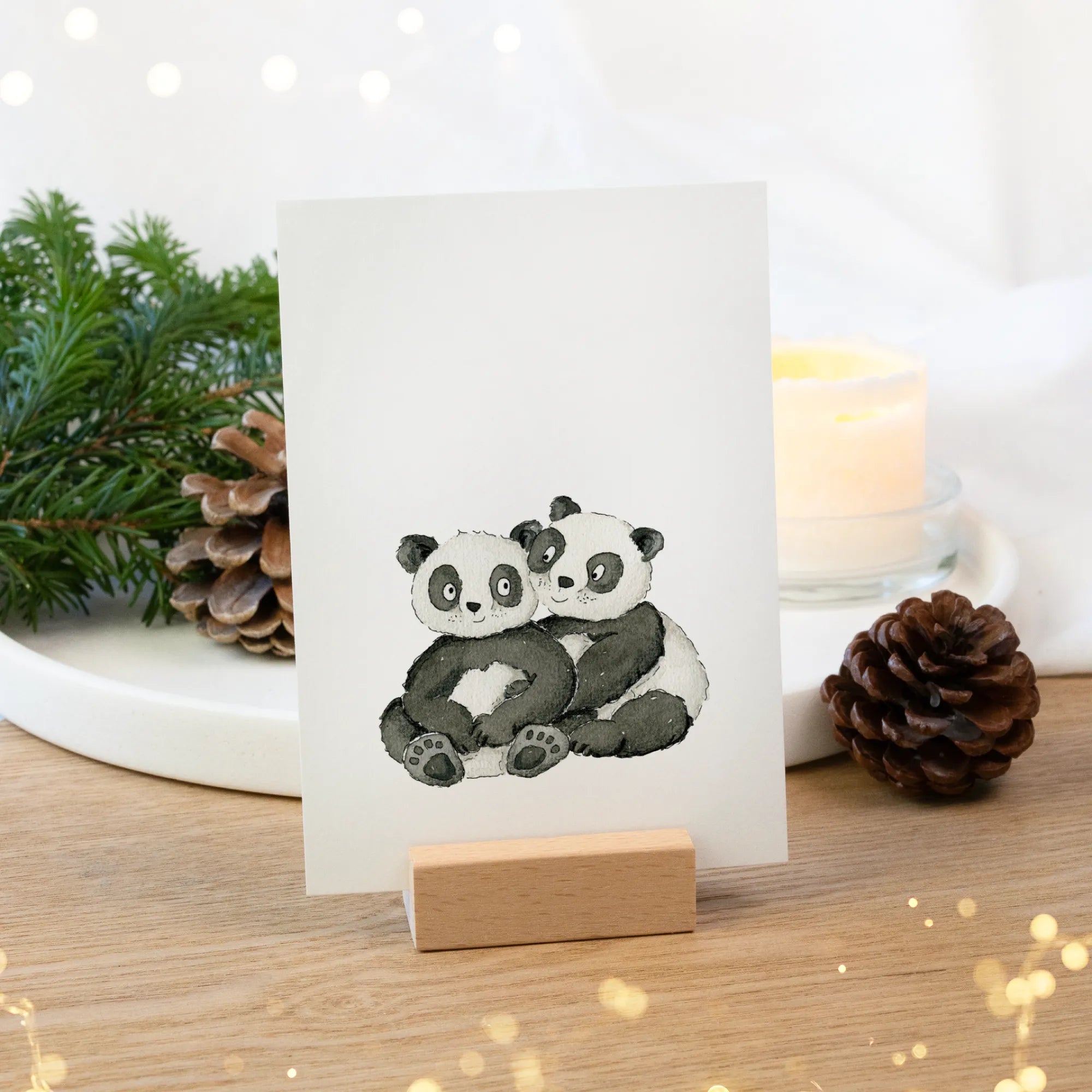 Eine Gutscheinkarte steht in einem Holz Kartenhalter. Darauf ein Panda Aquarell Motiv in schwarz und weiß gemalt.
