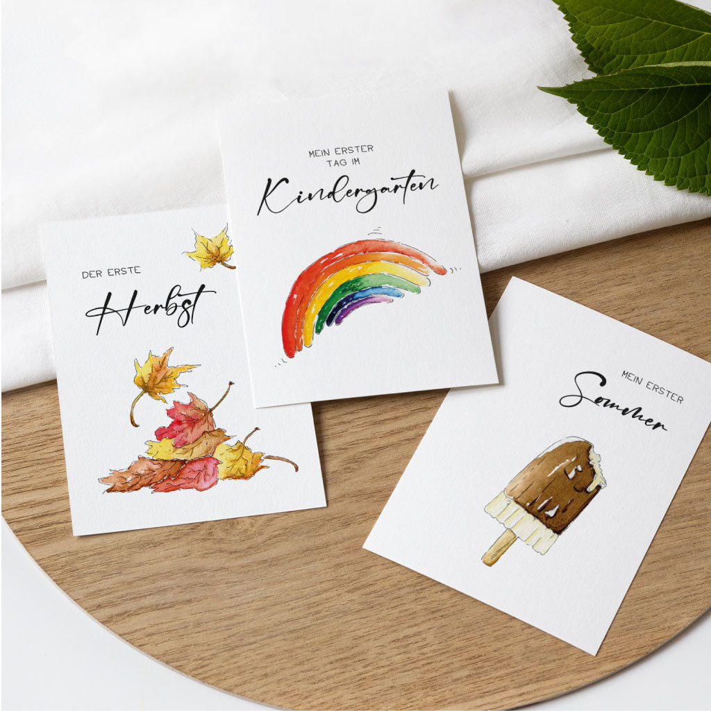 Drei Babykarten mit liebevoll handgemalten Aquarellen zu den Themen erster Herbst, erster Tag im Kindergarten und erster Sommer – ideal zur Erinnerung an besondere Entwicklungsschritte.