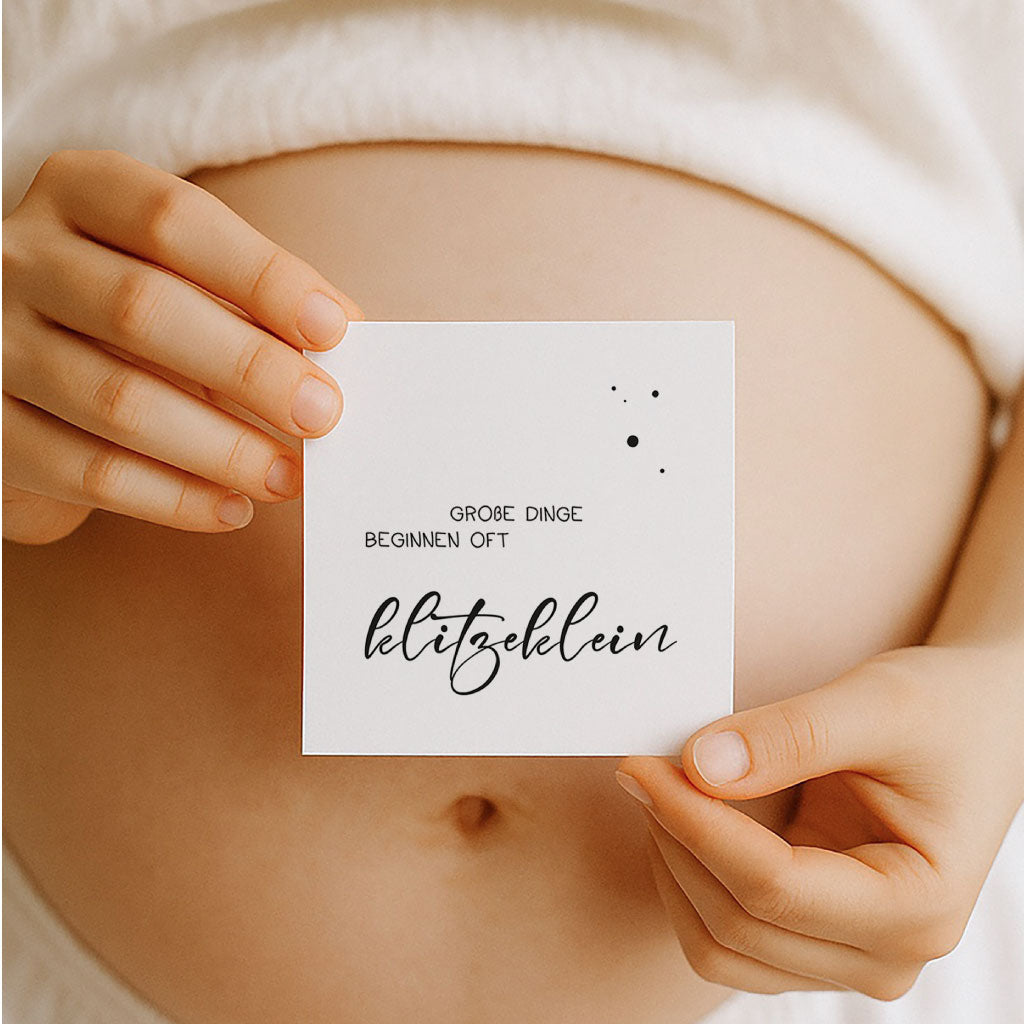 Schwangere hält eine minimalistische Meilensteinkarte mit der Aufschrift „Große Dinge beginnen oft klitzeklein“ – stilvolles Schwarz-Weiß-Design als PDF zum Ausdrucken, digitaler Download für werdende Mamas.