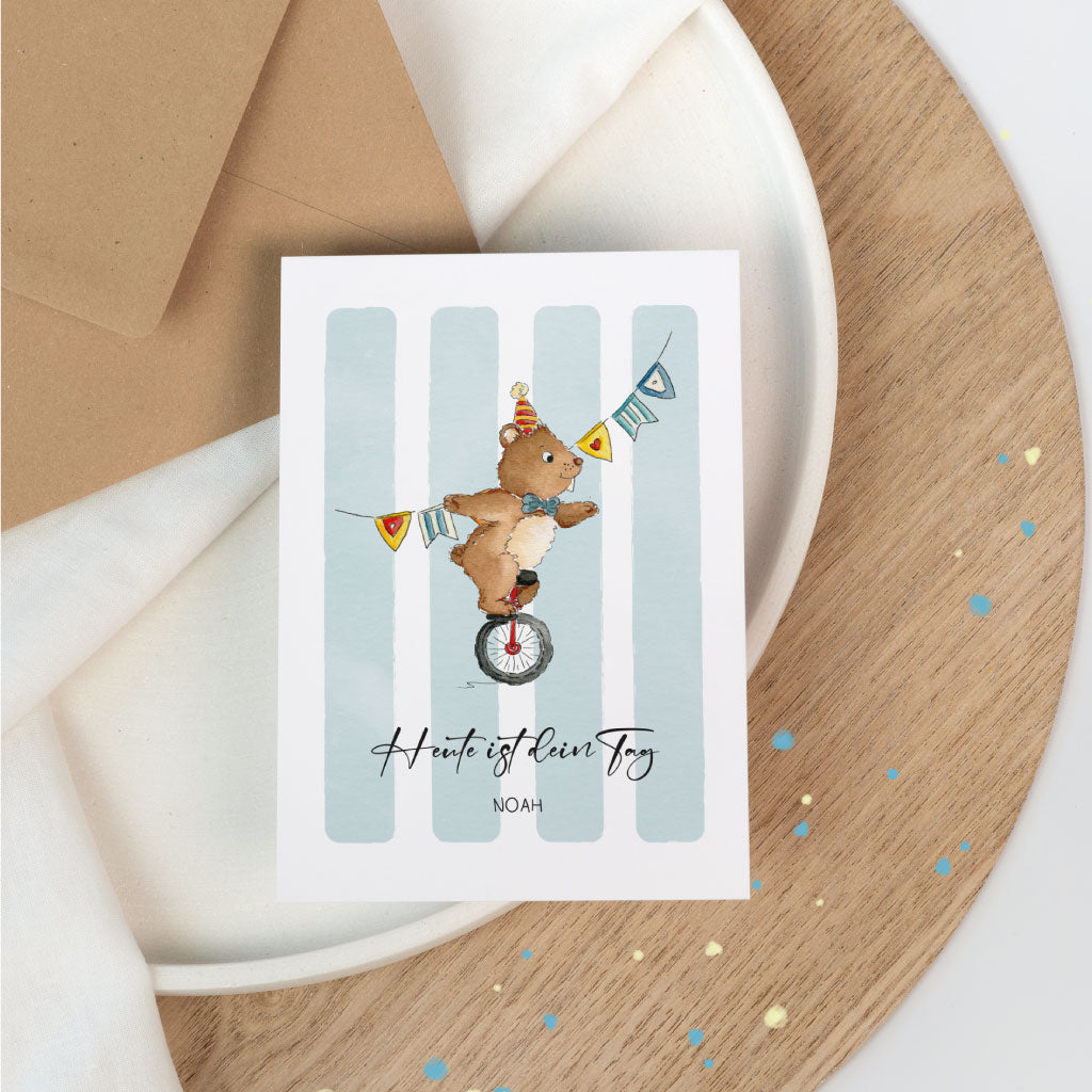 Geburtstagskarte im Zirkus-Stil mit handgemaltem Aquarellmotiv: ein Bär auf dem Einrad mit Wimpelkette, darunter personalisiert mit Name.