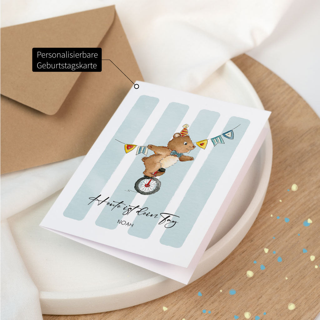 Personalisierbare Geburtstagskarte mit Aquarell-Bär auf Einrad, gestaltet im fröhlichen Zirkuslook mit Namensfeld und Schriftzug „Heute ist dein Tag“.