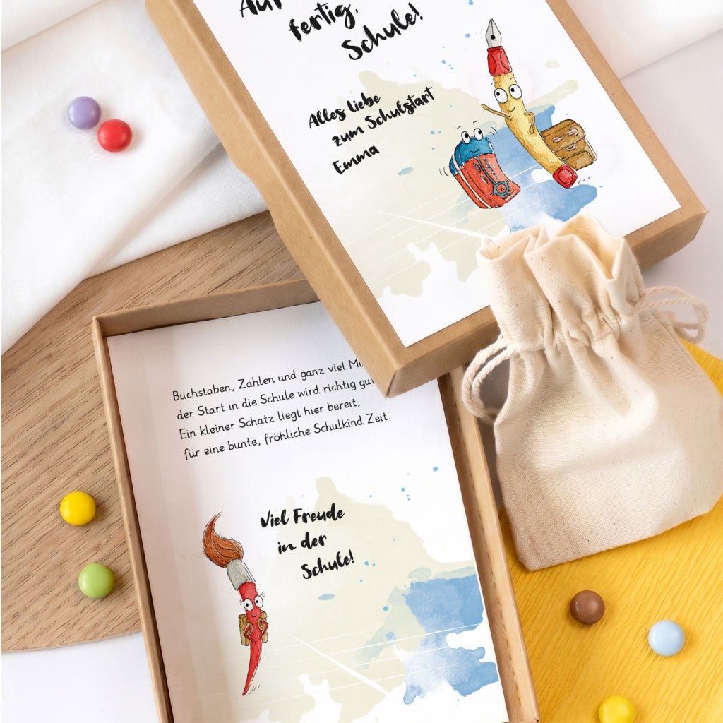 Geöffnete Geschenkschachtel zum Schulbeginn mit beigelegtem Säckchen und Pinsel Aquarell Motiv im Innenteil.