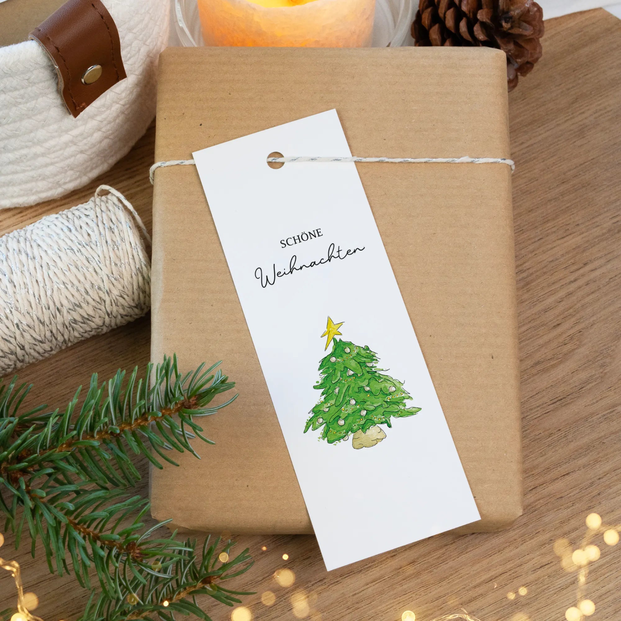 Ein langer Geschenkanhänger mit handgemaltem Weihnachtsbaum Aquarell Motiv liegt auf einem Geschenkpaket.