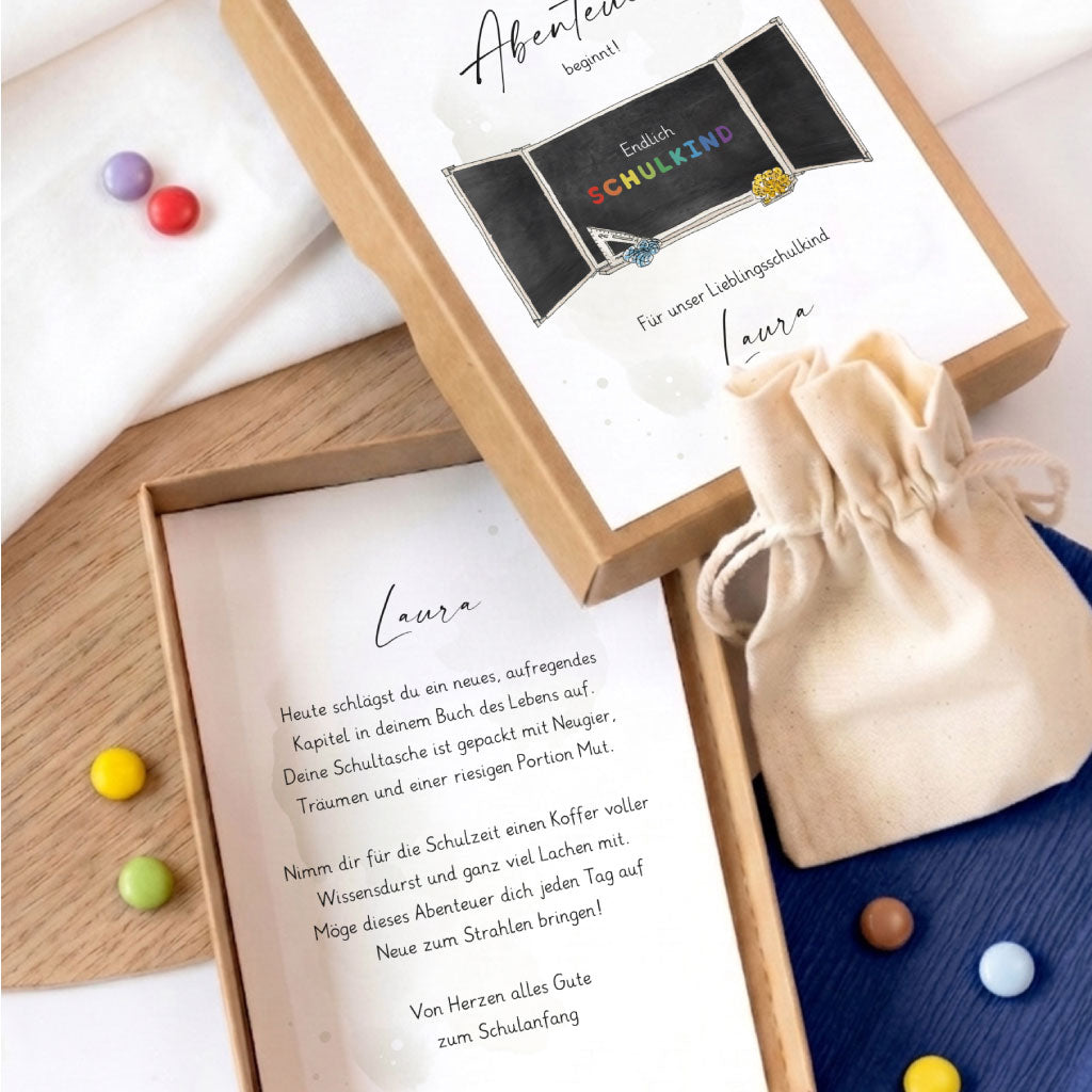Geöffnete Geschenkschachtel zur Einschulung mit personalisiertem Einlegetext und kleinem Beutel für ein Geldgeschenk.