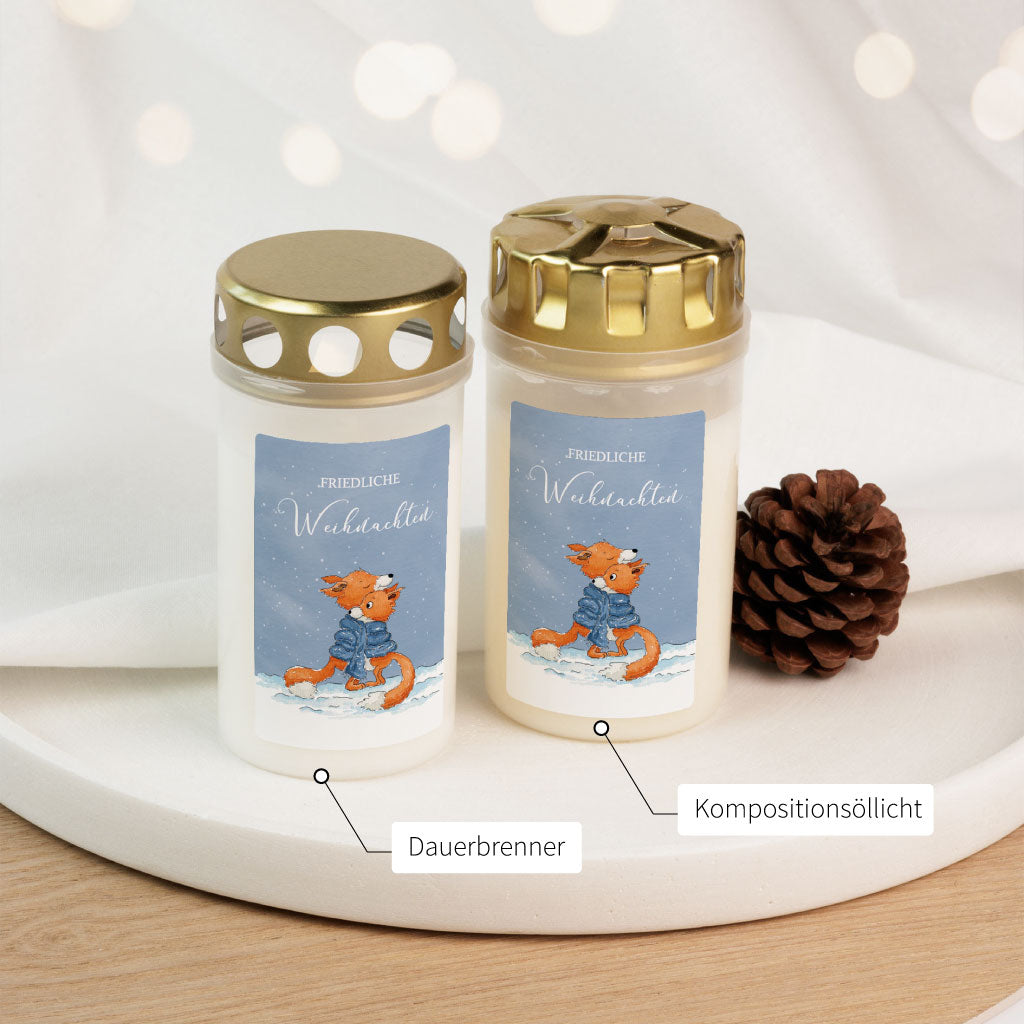 Zwei Grabkerzen im Vergleich: Dauerbrenner und Kompositionsölllicht, beide mit winterlichem Fuchs-Aufkleber und Schriftzug "Friedliche Weihnachten".