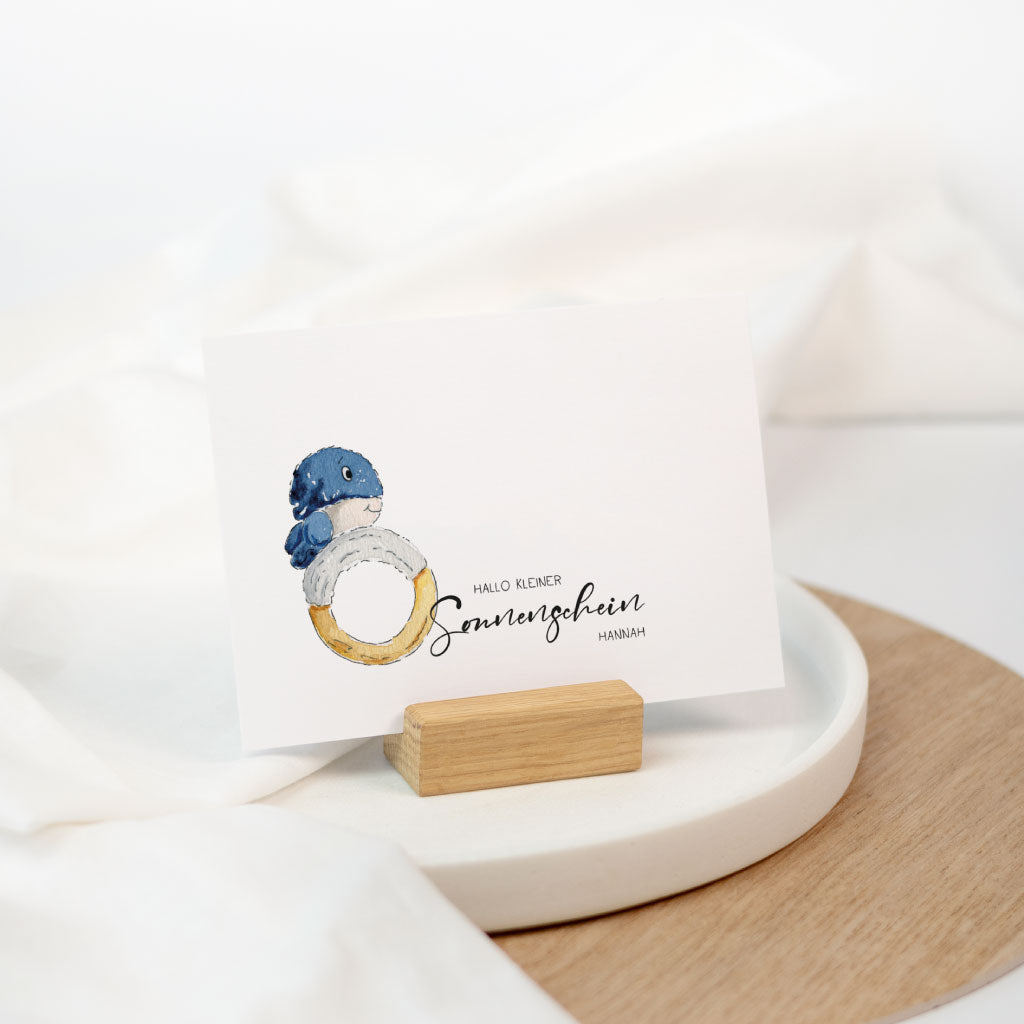 Aufgestellte Geburt Baby Glückwunschkarte: personalisierbar mit Name, Wal-Baby Motiv auf weißer Karte in einem kleinen Holzhalter.