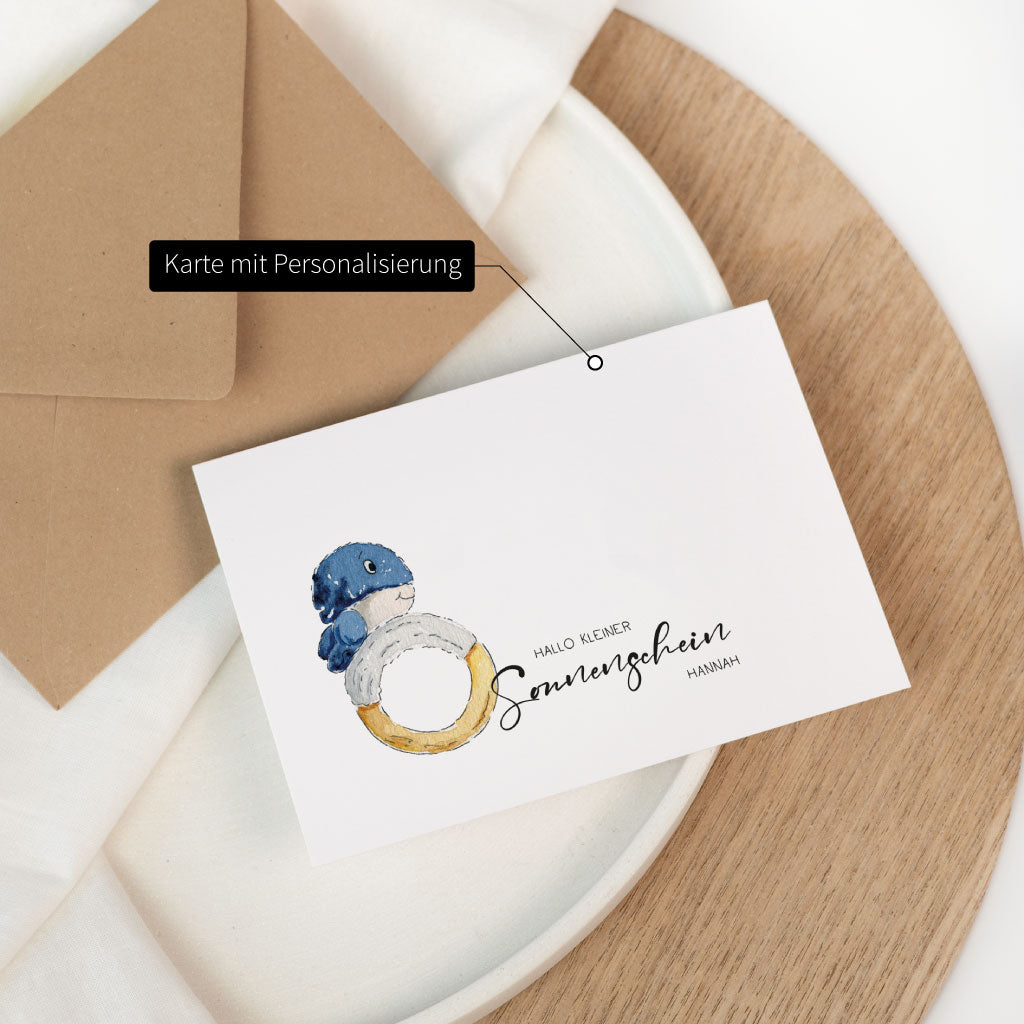 Personalisierbare Glückwunschkarte zur Geburt eines Baby mit Wal-Baby Motiv, beschriftet als „Karte mit Personalisierung“, dekorativ neben Umschlag fotografiert.