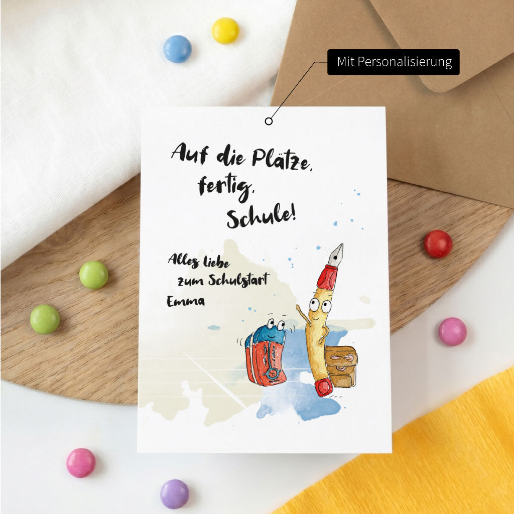Personalisierte Karte Einschulung mit Name Emma und lustigem Stifte Aquarell Motiv auf einem Holztisch.