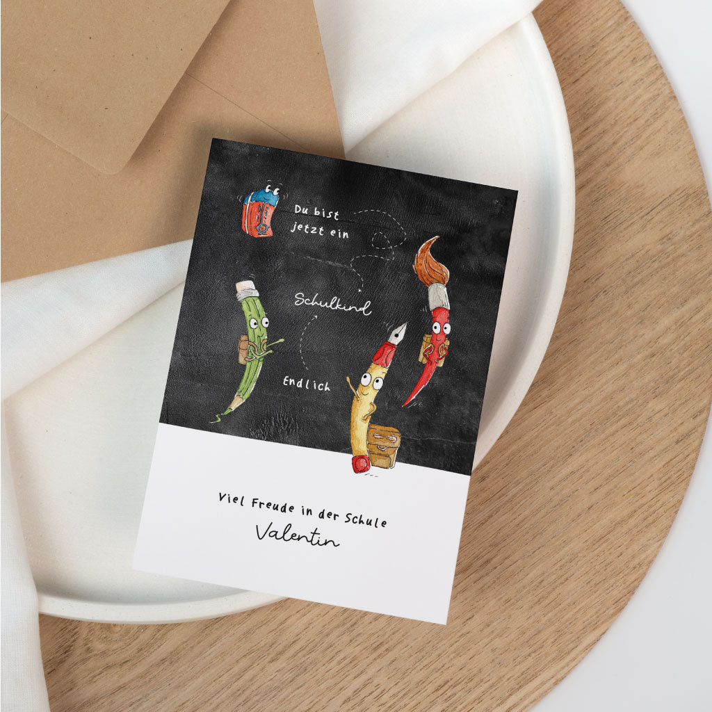 Motiv: Füller, Pinsel, Buntstift und Radiergummi auf einer Schultafel mit Text "Du bist jetzt ein Schulkind! Endlich!"