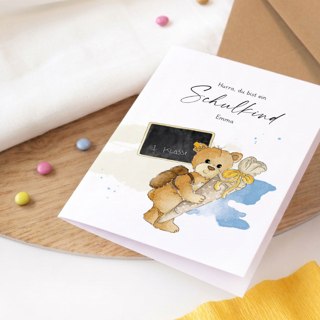 Personalisierte Karte zum Schulanfang auf Holzplatte mit niedlichem Teddy Aquarell Motiv und bunten Linsen.