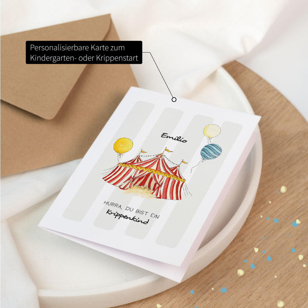 Aufgeklappte, personalisierbare Karte für Krippe oder Kindergarten Anfang mit Zirkus-Aquarellmotiv, Name „Emilio“ und Schriftzug „Hurra, du bist ein Krippenkind“