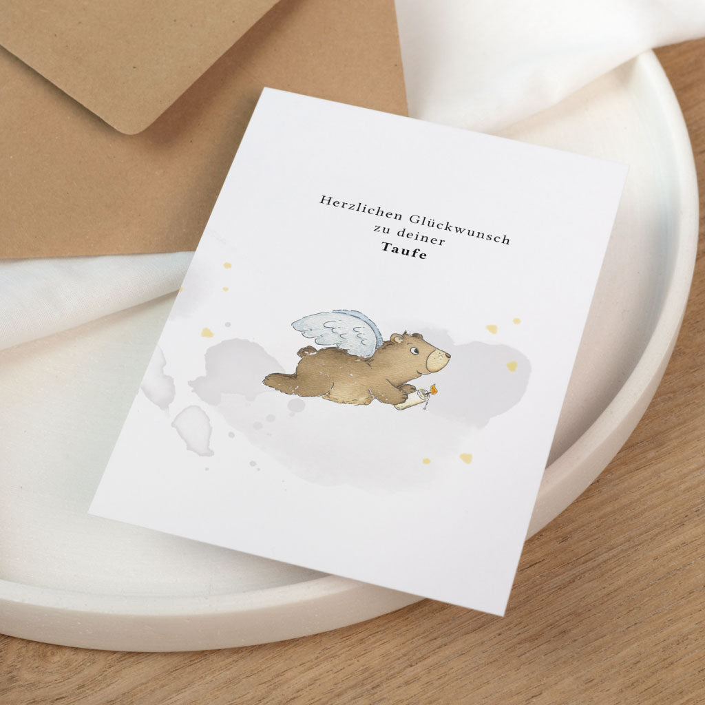 Personalisierbare Glückwunschkarte zur Taufe mit handgemaltem Bärenmotiv auf weißer Klappkarte neben Kraftpapierumschlag