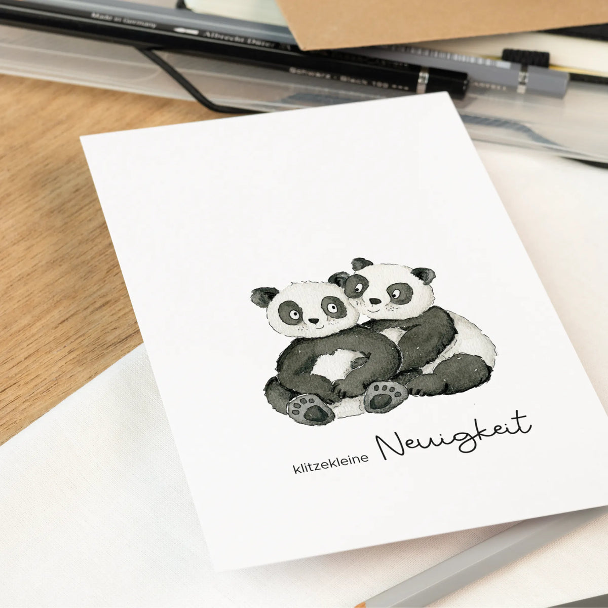 Nahaufnahme der Schwangerschaftskarte mit zwei sich umarmenden handgemalten Pandas und Schriftzug klitzekleine Neuigkeit