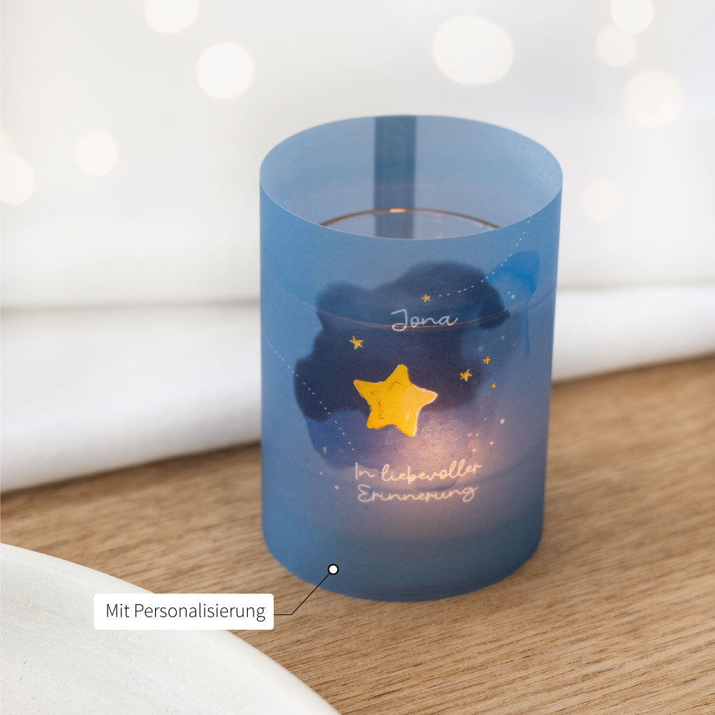 Nahaufnahme eines leuchtenden Teelichts in einer Trauer-Lichthülle mit Sternen und Name – personalisierbares Trostgeschenk für stille Gedenkmomente.