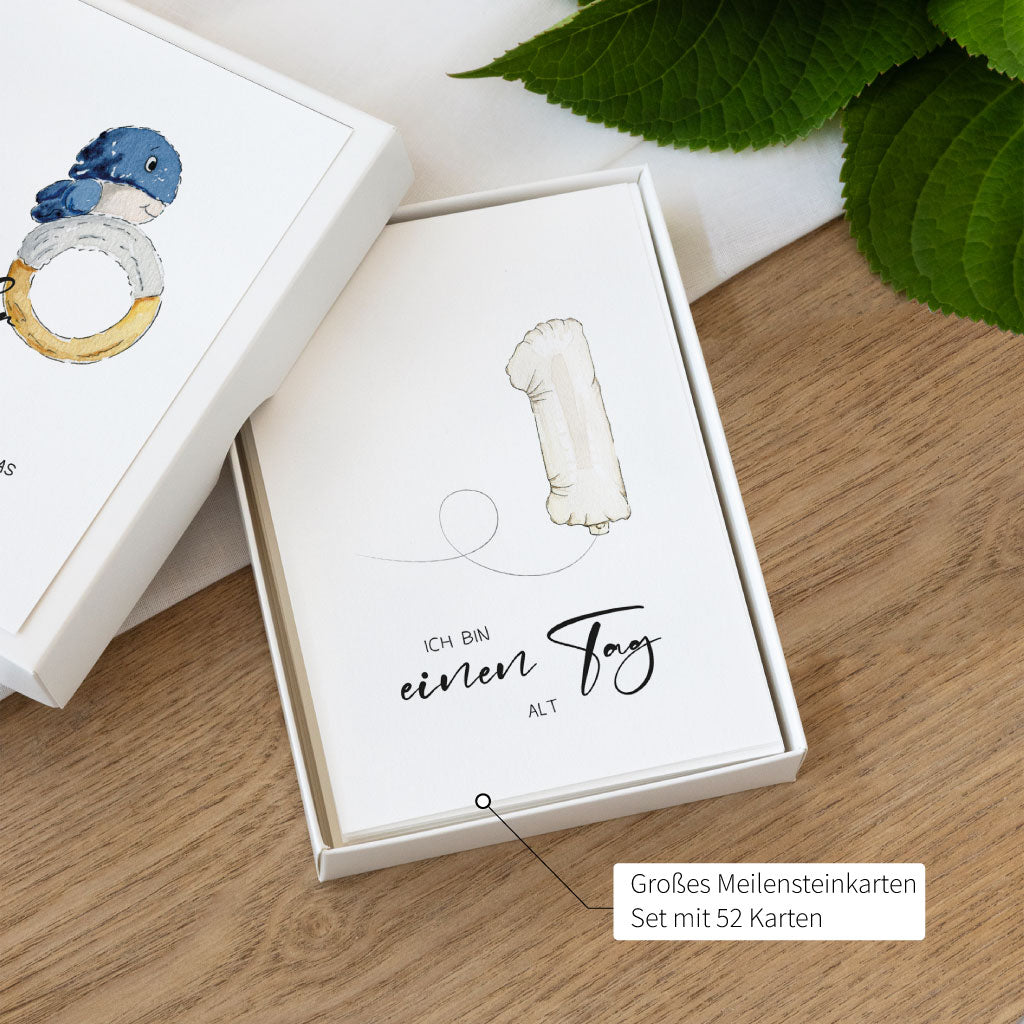 Geöffnete Geschenkbox mit Meilensteinkarte „Ich bin einen Tag alt“, Teil eines 52-teiligen Sets für Wochenkarten und Monatskarten im ersten Babyjahr.