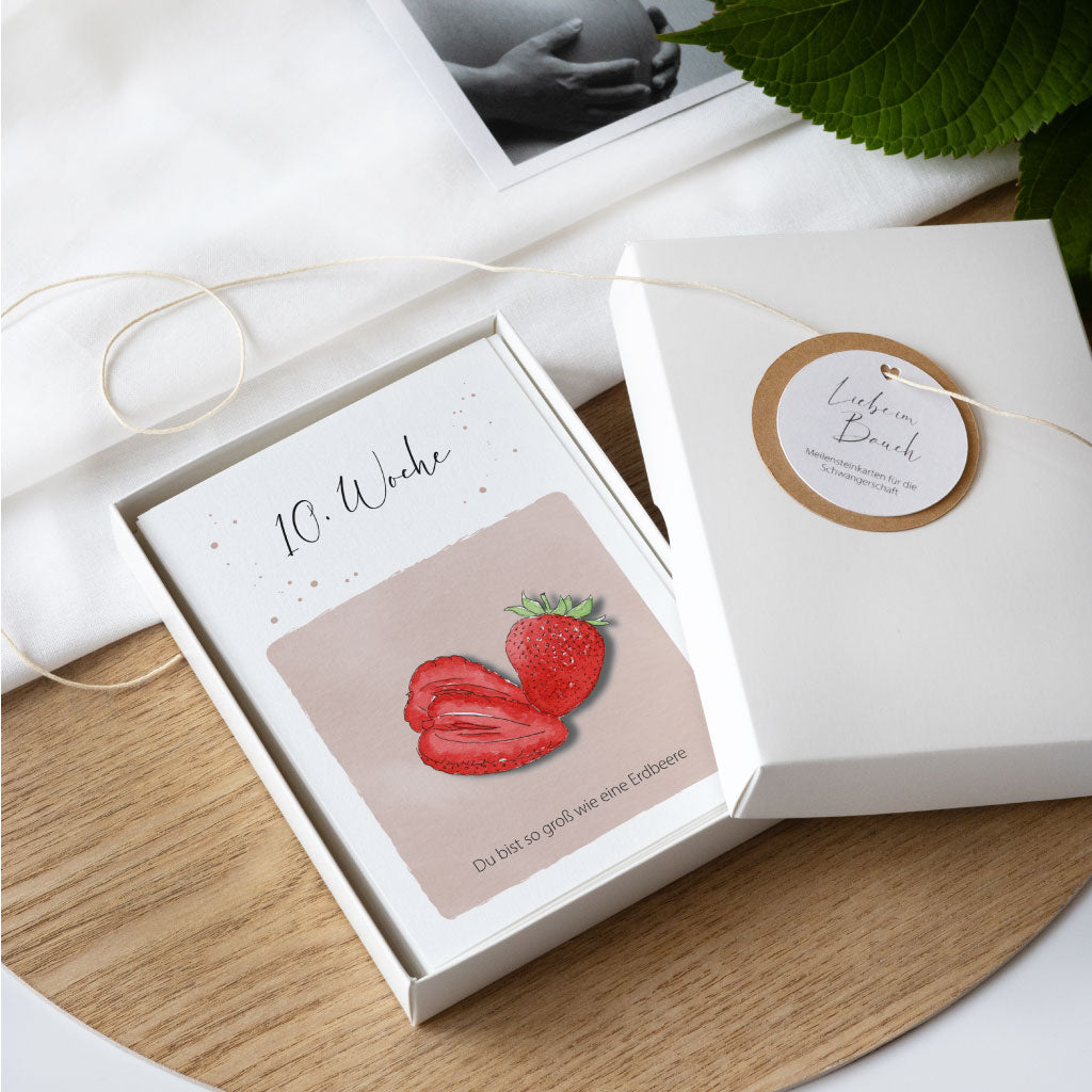 Meilensteinkarten Schwangerschaft, Geschenkschachtel geöffnet, darauf Anhänger "Liebe im Bauch"