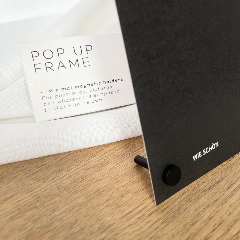 Pop Up Frame Kartenständer in magnetisch schwarz mit Karte „WIE SCHÖN“, daneben die Verpackung – Fotohalter für Karten und Fotos.