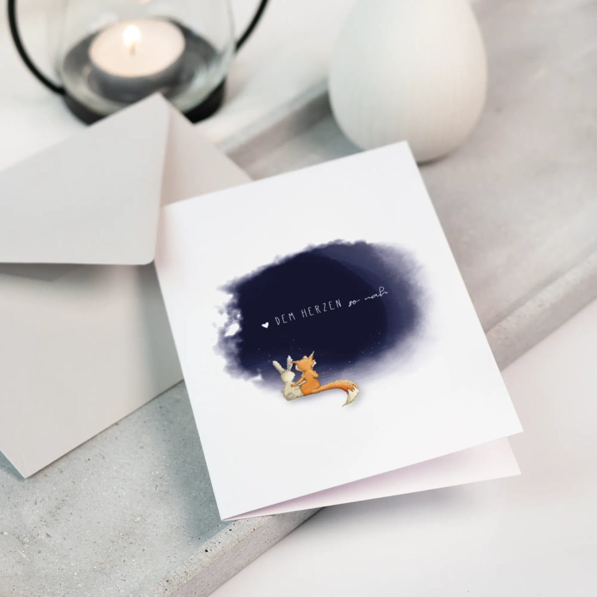 Trauerkarte Dem Herzen so nah mit Fuchs und Hase im Aquarell, aufgestellt neben Umschlag und Teelicht, Trauergeschenk