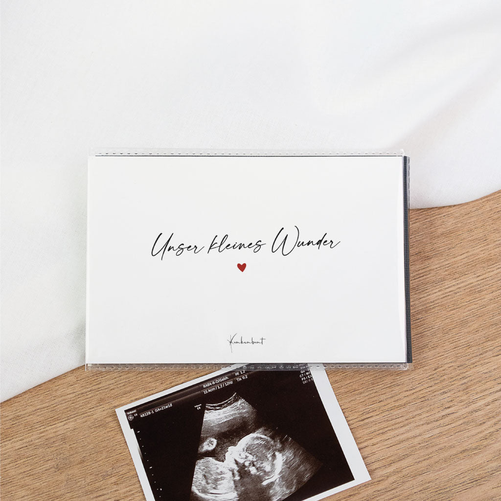 Ultraschallbilder Aufbewahrung Album: weißes Einsteckalbum „Unser kleines Wunder“ mit kleinem Herz, darunter ein Ultraschallfoto – schwarzes Album als Schutz für Ultraschall Fotos.
