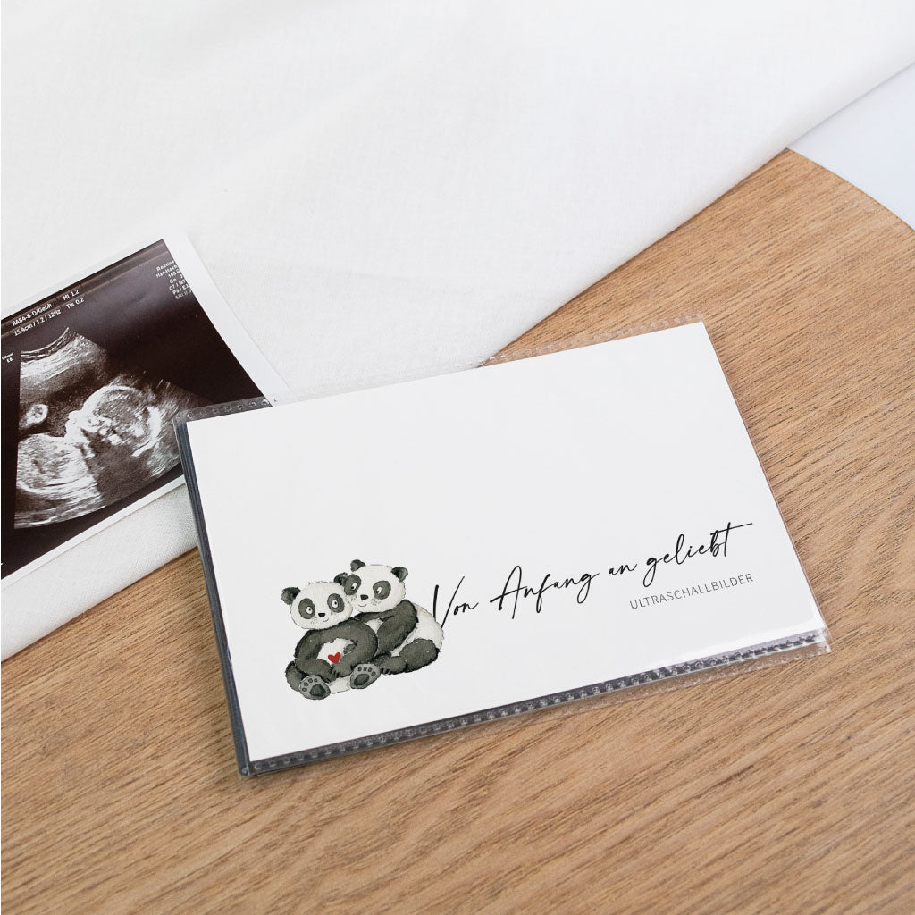 Ultraschallbilder Aufbewahrung: Einsteckalbum „Von Anfang an geliebt“ mit handgemalten Pandas, daneben Ultraschallfoto auf Holztisch – personalisierbar als Schwangerschaft Geschenk.