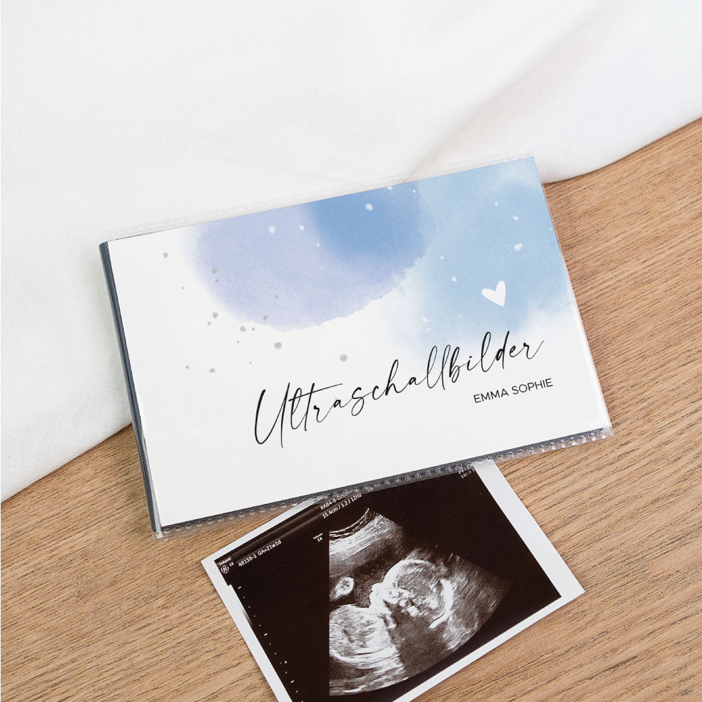 Schwarzes Einsteckalbum zur Ultraschallbilder Aufbewahrung, auf Holzuntergrund mit Ultraschallfoto – Cover in Blau mit Schriftzug „Ultraschallbilder“, personalisierbar mit Name