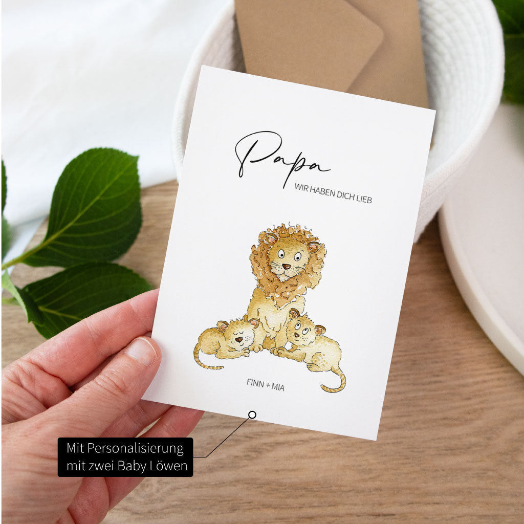 Hand hält eine personalisierte Vatertagskarte mit einem Papa Löwen und zwei kleinen Löwenkindern im hellen Tageslicht.