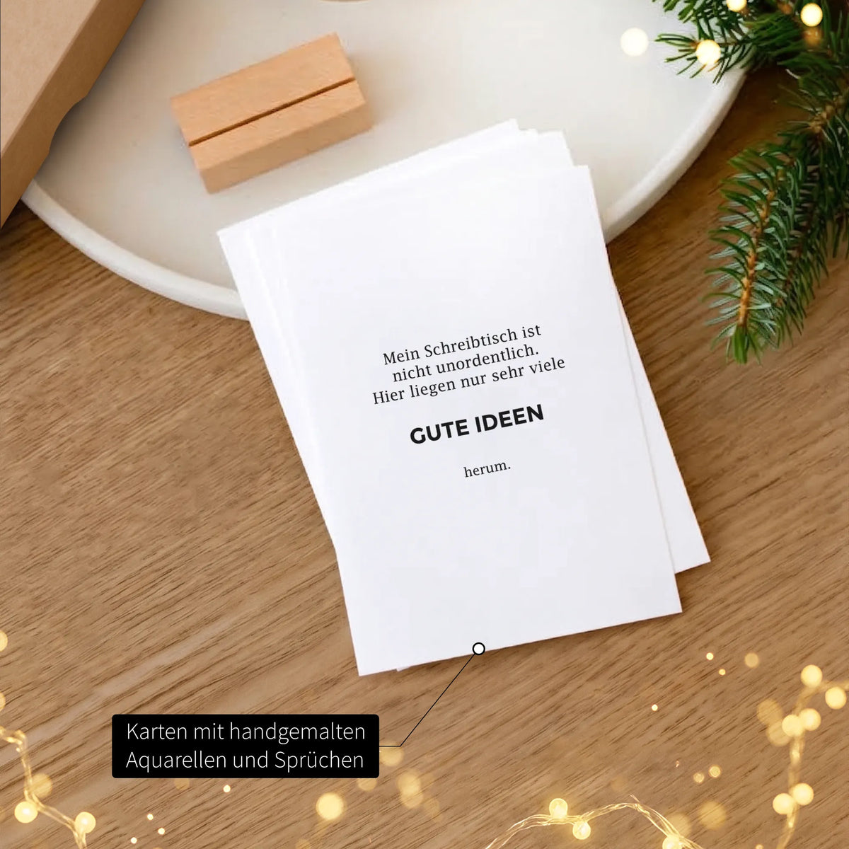 Karte mit humorvollem Spruch Gute Ideen aus dem Weihnachtsgeschenk-Set, Holz-Kartenhalter im Hintergrund, weihnachtliche Lichterkette