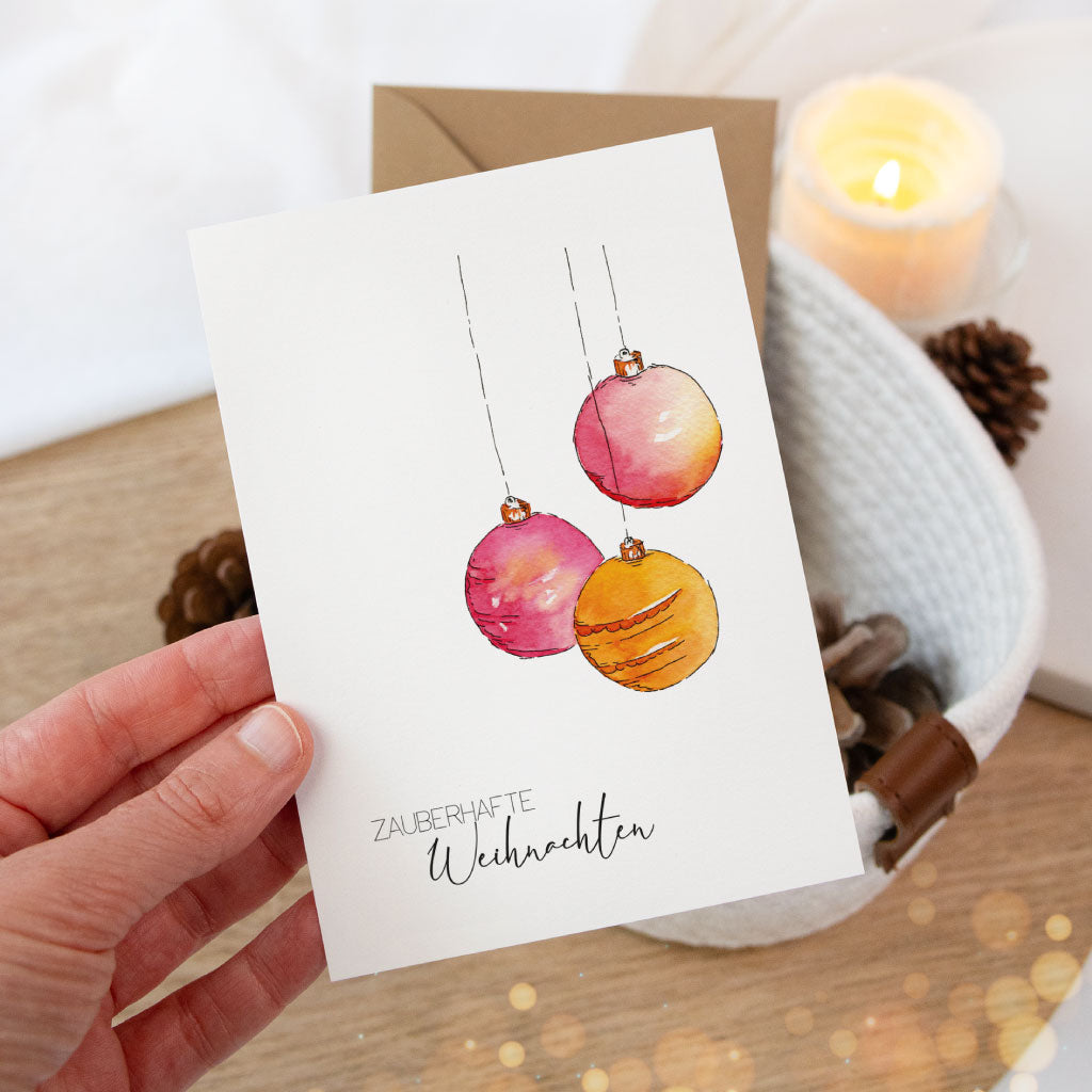 Künstlerisch illustrierte Weihnachtskarte mit hängenden Christbaumkugeln und handgeschriebenem Grußtext, perfekt für persönliche Weihnachtsgrüße.