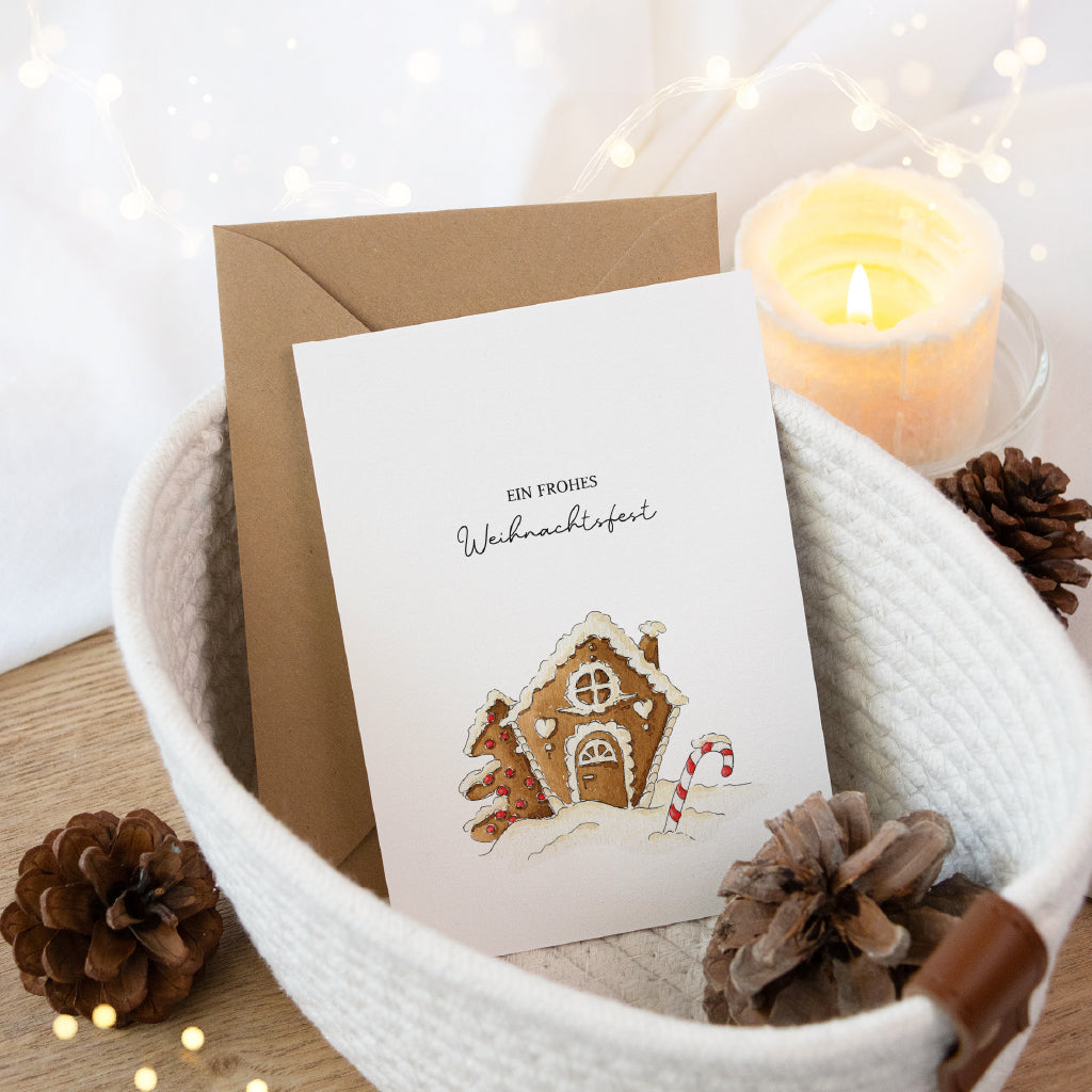 Weihnachtskarte mit Lebkuchenhaus Aquarell Motiv liegend in einem weißen geflochtenen Korb.