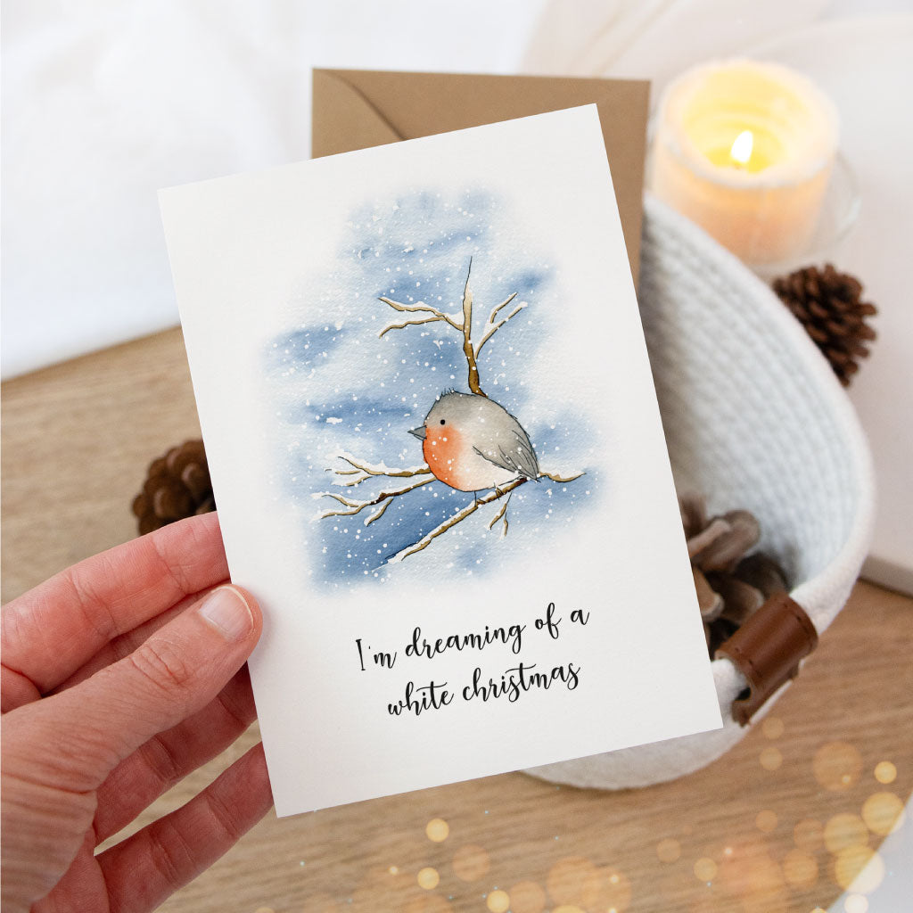 Weihnachtskarte mit liebevoll gemaltem Rotkehlchen im Schnee, in einer Hand gehalten – winterliche Illustration mit Spruch für persönliche Weihnachtsgrüße.