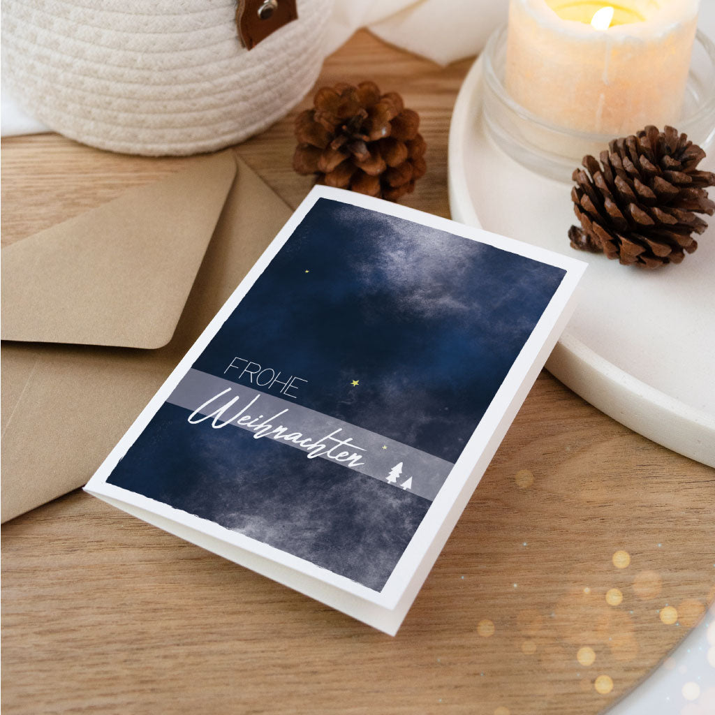 Künstlerische Klappkarte mit winterlichem Aquarellmotiv in Blau und der Aufschrift „Frohe Weihnachten“, ideal zum Weihnachtsgeschenke verpacken und Verschenken.