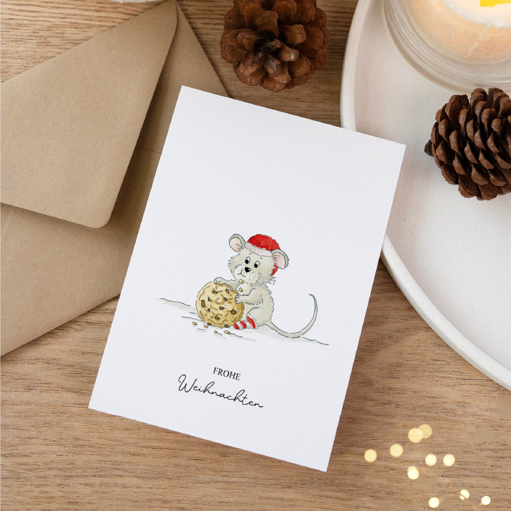 Handgemaltes Maus Aquarell Motiv auf einer weißen Klappkarte für liebevolle Weihnachtspost neben Tannenzapfen.