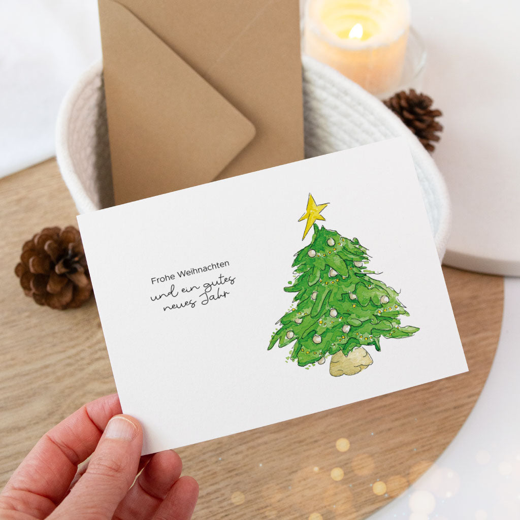 Hand hält eine liebevoll gestaltete Weihnachtskarte mit festlich geschmücktem Baum und Neujahrswunsch – perfekt zum Schreiben von Weihnachtsgrüßen oder für Geschenkverpackungen.