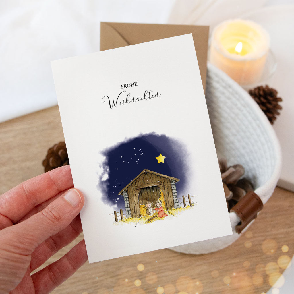 Hand hält eine festliche Klappkarte mit weihnachtlichem Krippenmotiv aus Aquarell – hochwertige Weihnachtskarte mit christlichem Bezug.